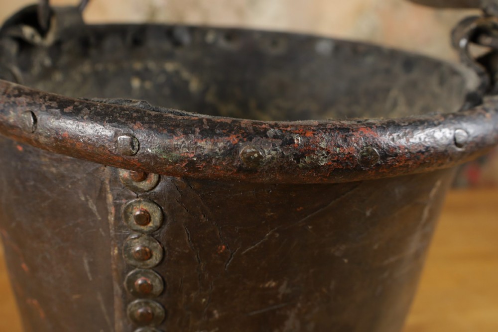 A dark brown Georgian leather fire bucket featuring a heavy strap handle, brass studs around the base, and a painted royal coat of arms with a lion and unicorn. View XI