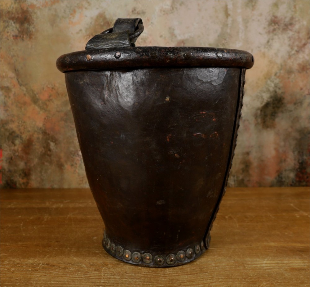 A dark brown Georgian leather fire bucket featuring a heavy strap handle, brass studs around the base, and a painted royal coat of arms with a lion and unicorn. View XII