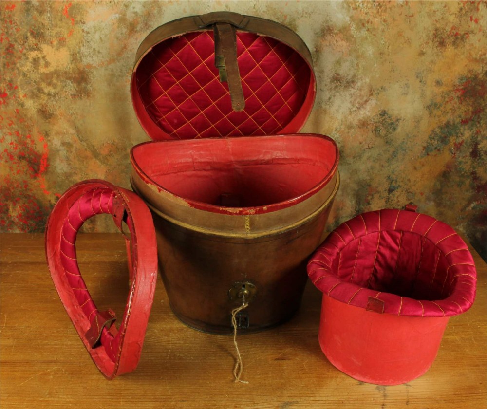 An open Victorian brown leather hat case featuring a padded bright red quilted silk lining and removable hat support collars.