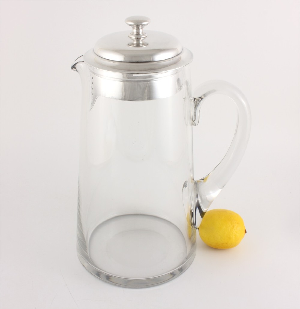 A clear glass water jug with a silver-plated hinged lid, integrated strainer spout, and curved glass handle. View II