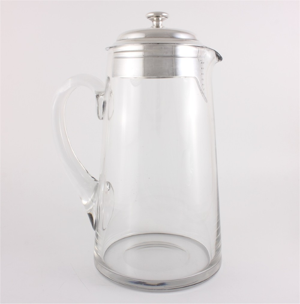 A clear glass water jug with a silver-plated hinged lid, integrated strainer spout, and curved glass handle. View III