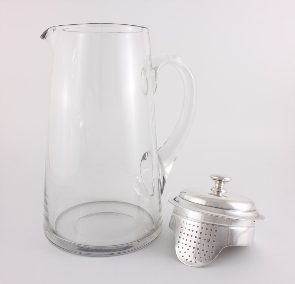 A clear glass water jug with a silver-plated hinged lid, integrated strainer spout, and curved glass handle. View IV