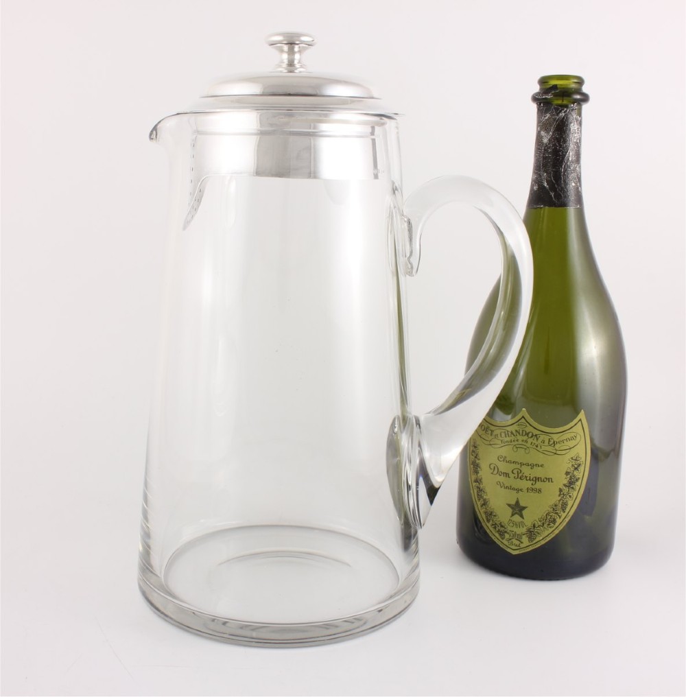 A clear glass water jug with a silver-plated hinged lid, integrated strainer spout, and curved glass handle. View VI