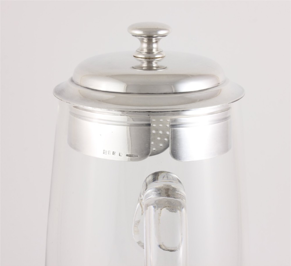 A clear glass water jug with a silver-plated hinged lid, integrated strainer spout, and curved glass handle. View XIII