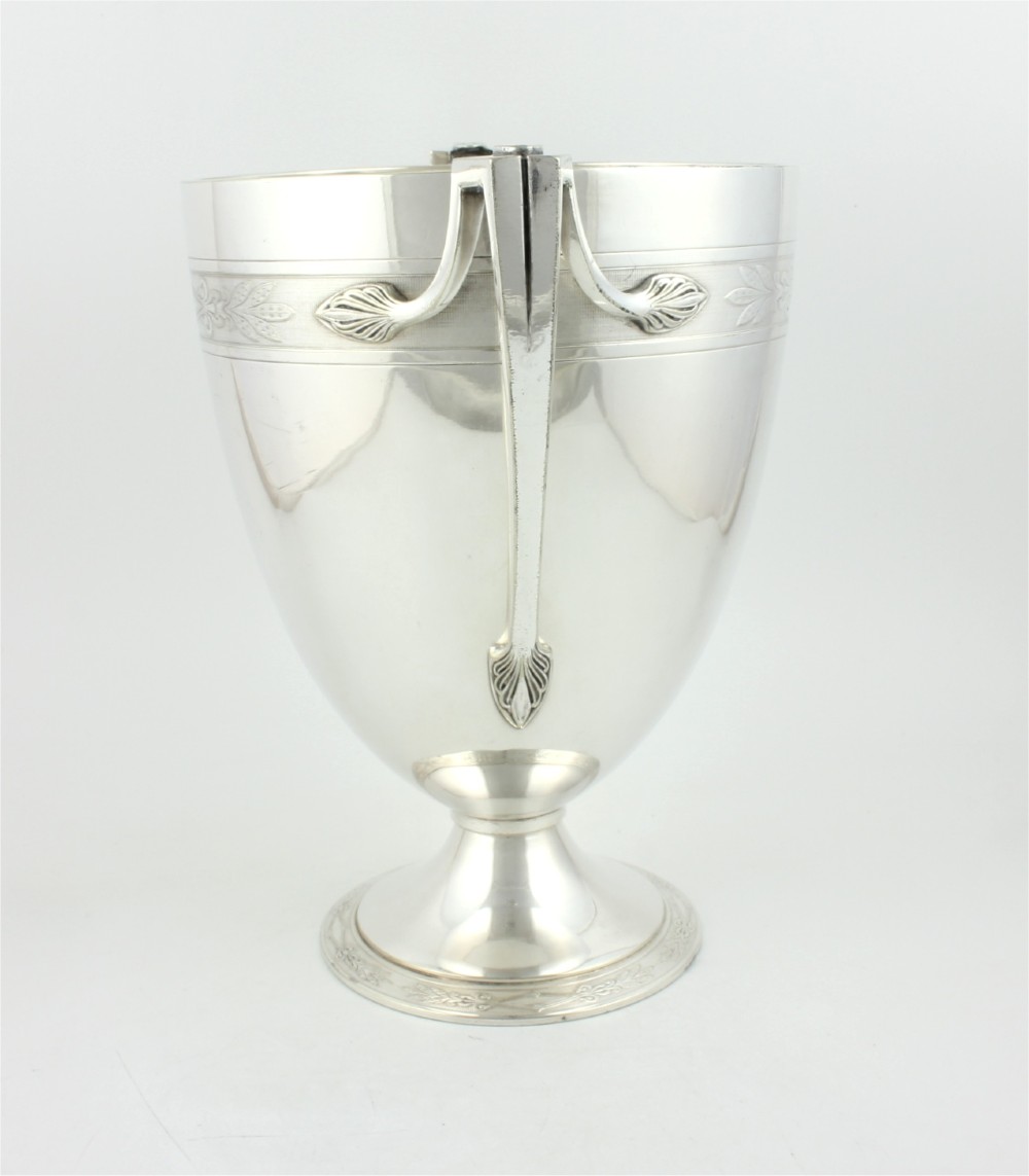 An antique silver-plated urn-shaped champagne cooler featuring twin angular handles, a foliage engraved band, and a stepped pedestal foot. View III