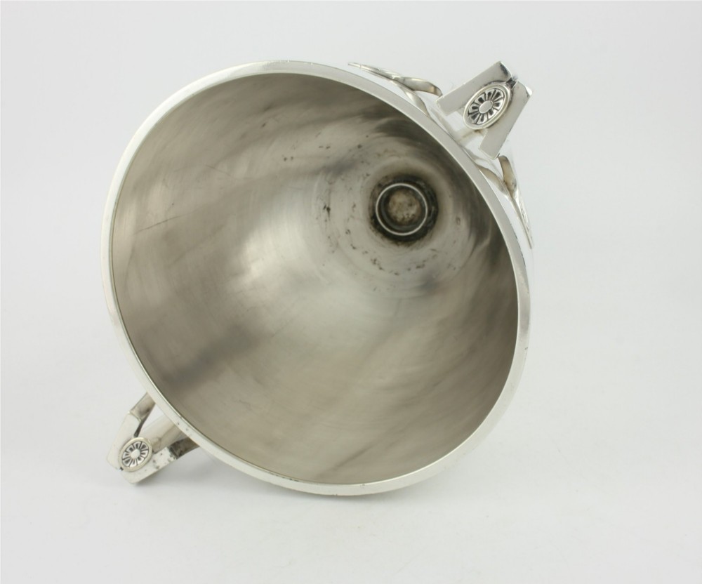 An antique silver-plated urn-shaped champagne cooler featuring twin angular handles, a foliage engraved band, and a stepped pedestal foot. View XI
