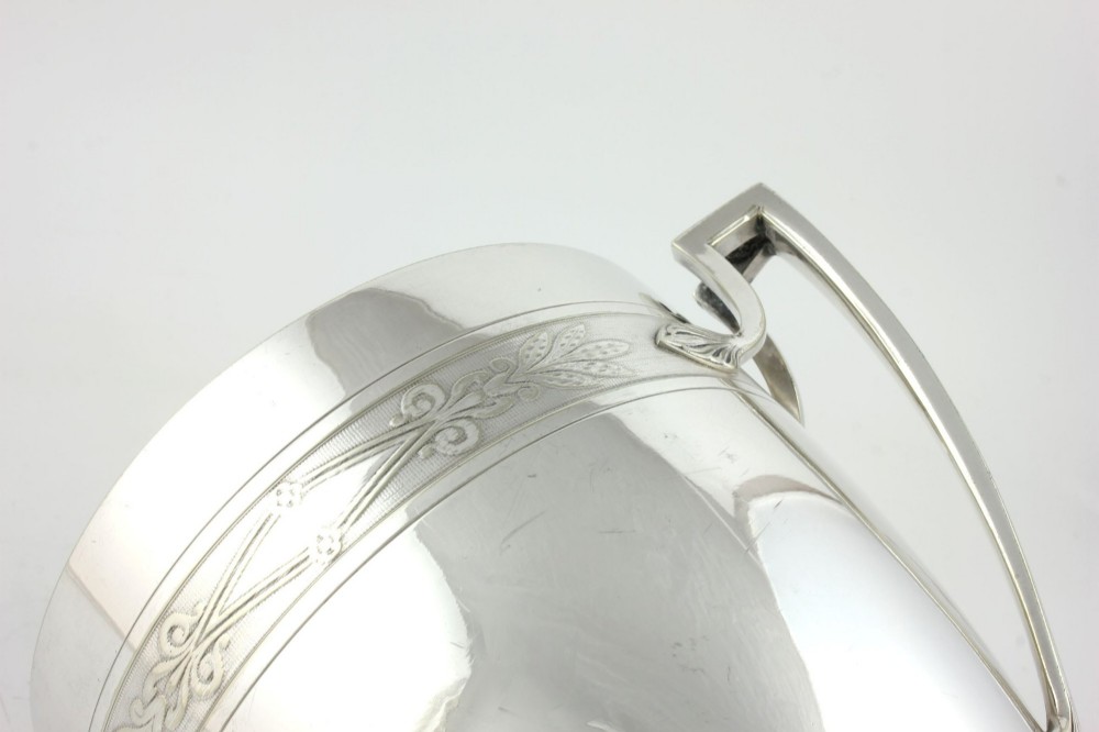 An antique silver-plated urn-shaped champagne cooler featuring twin angular handles, a foliage engraved band, and a stepped pedestal foot. View XII