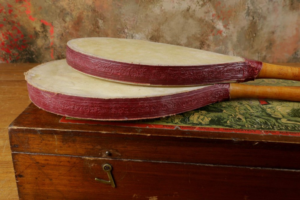 An open wooden pine box containing two vellum ping pong rackets, a white ball, and brass net clamps with a folded green net, featuring a Hamleys paper label inside the lid. View XII