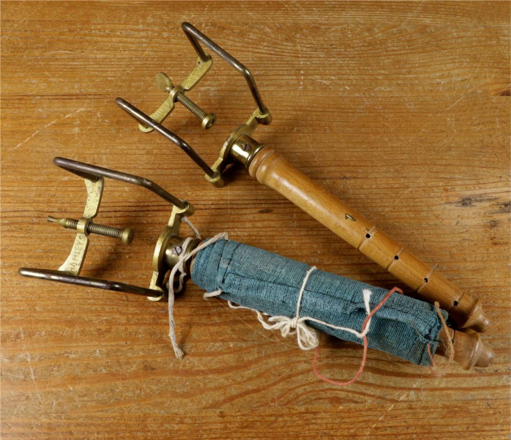 An open wooden pine box containing two vellum ping pong rackets, a white ball, and brass net clamps with a folded green net, featuring a Hamleys paper label inside the lid. View XV