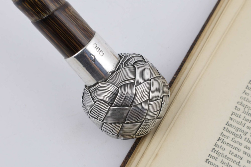 A close-up of an antique walking stick featuring a woven silver wire knot handle mounted on a dark bamboo shaft with a silver collar. View VI