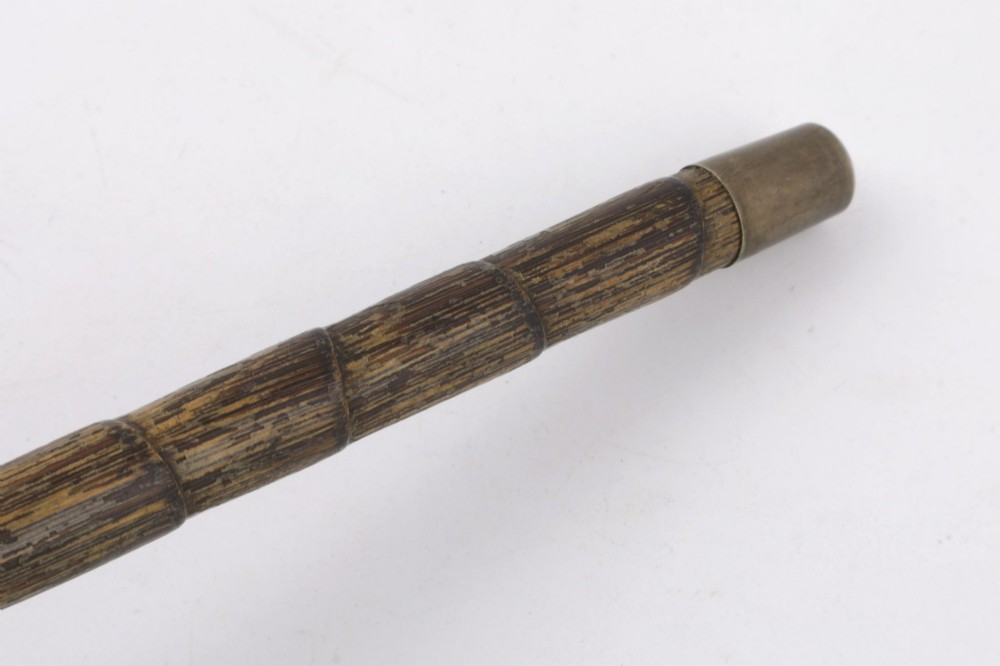 A close-up of an antique walking stick featuring a woven silver wire knot handle mounted on a dark bamboo shaft with a silver collar. View IX