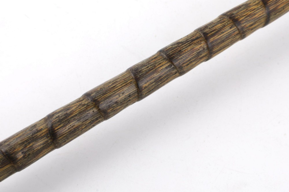 A close-up of an antique walking stick featuring a woven silver wire knot handle mounted on a dark bamboo shaft with a silver collar. View X