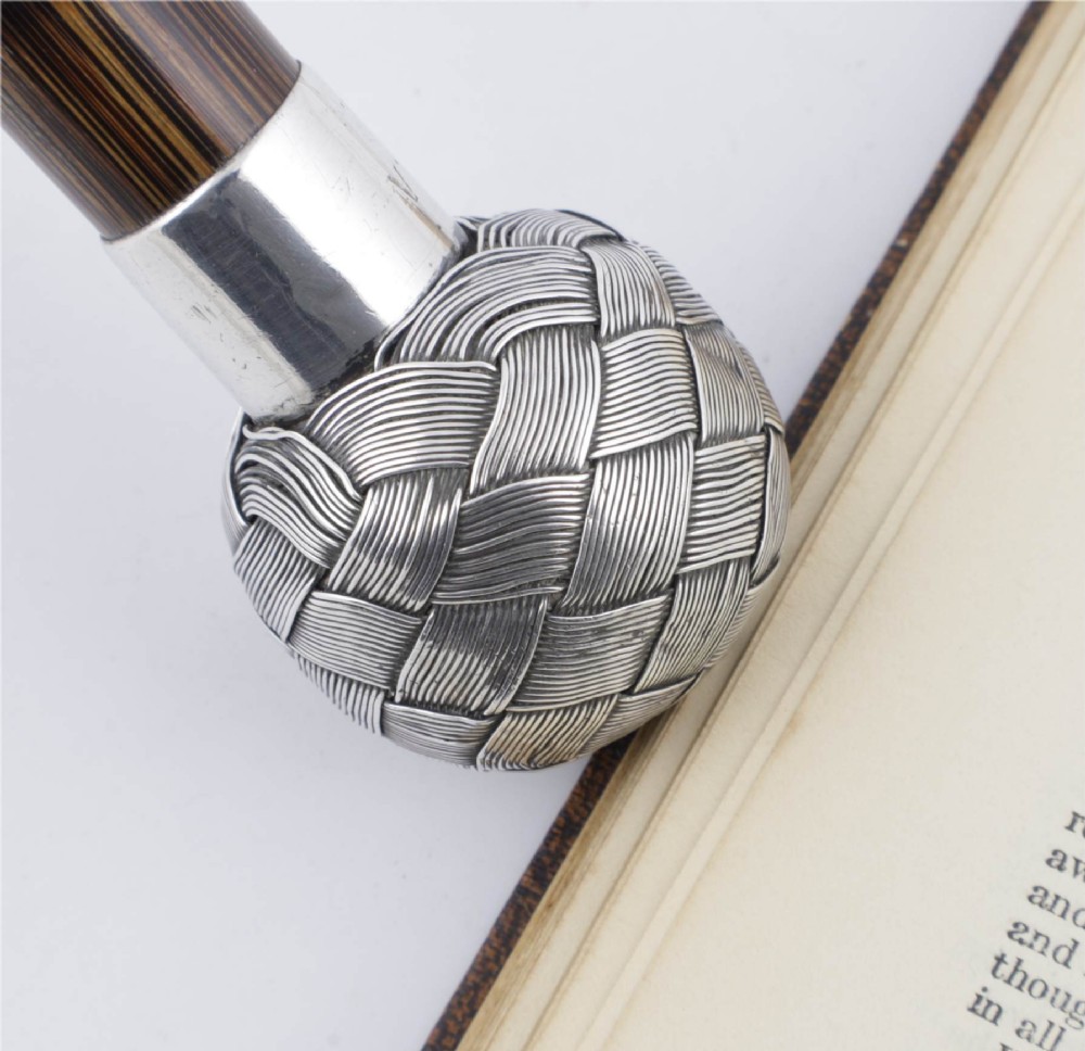 A close-up of an antique walking stick featuring a woven silver wire knot handle mounted on a dark bamboo shaft with a silver collar. View XI