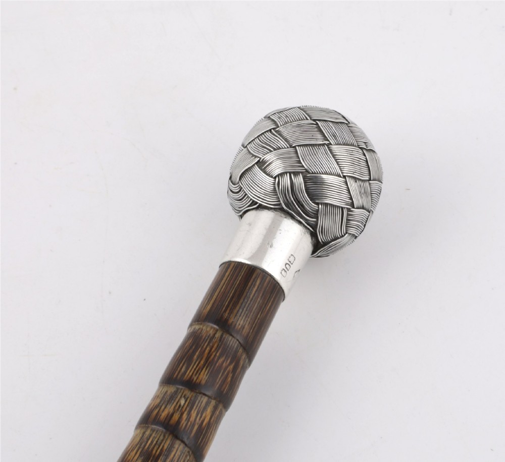 A close-up of an antique walking stick featuring a woven silver wire knot handle mounted on a dark bamboo shaft with a silver collar. View XII