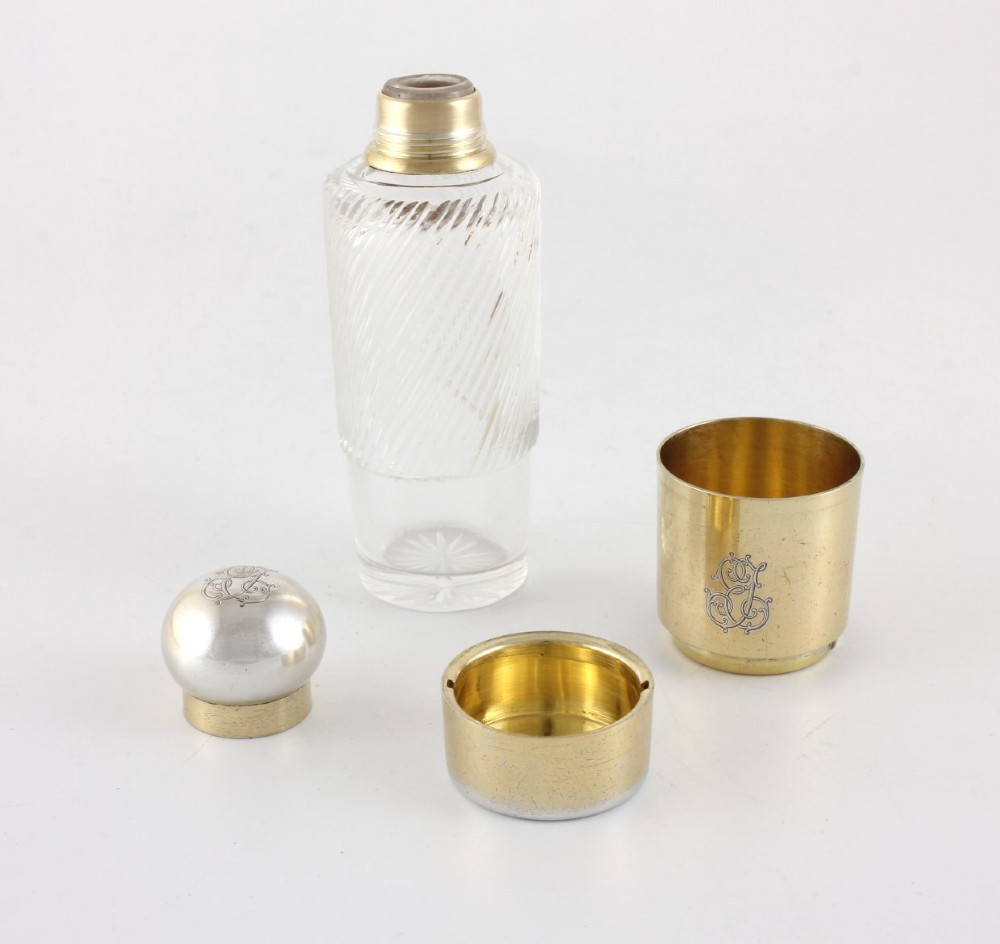 A cylindrical clear glass flask featuring spiral fluting, topped with a domed silver cap and a silver base bearing an engraved monogram. View II