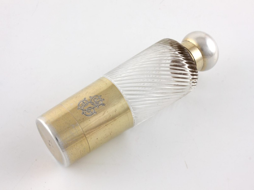 A cylindrical clear glass flask featuring spiral fluting, topped with a domed silver cap and a silver base bearing an engraved monogram. View VII