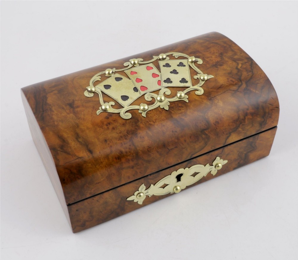 A domed burr walnut box featuring polished brass strapwork depicting three playing cards on the lid and a brass keyhole escutcheon on the front. View V