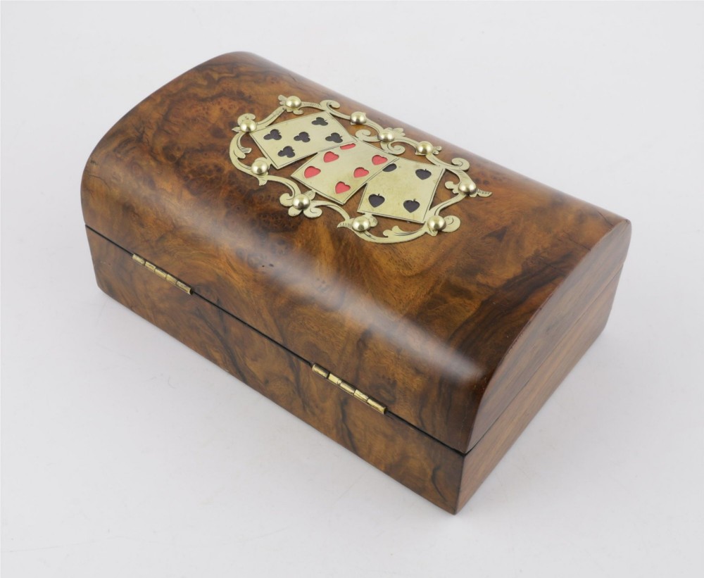 A domed burr walnut box featuring polished brass strapwork depicting three playing cards on the lid and a brass keyhole escutcheon on the front. View VI