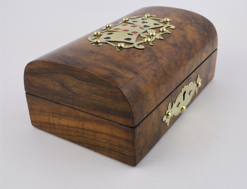 A domed burr walnut box featuring polished brass strapwork depicting three playing cards on the lid and a brass keyhole escutcheon on the front. View XII