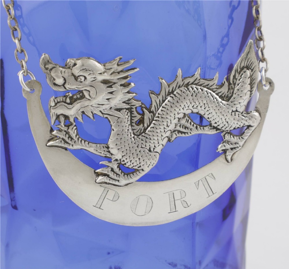 An antique Chinese silver decanter label depicting a chased dragon above a crescent plaque engraved with PORT, attached to a chain. View II