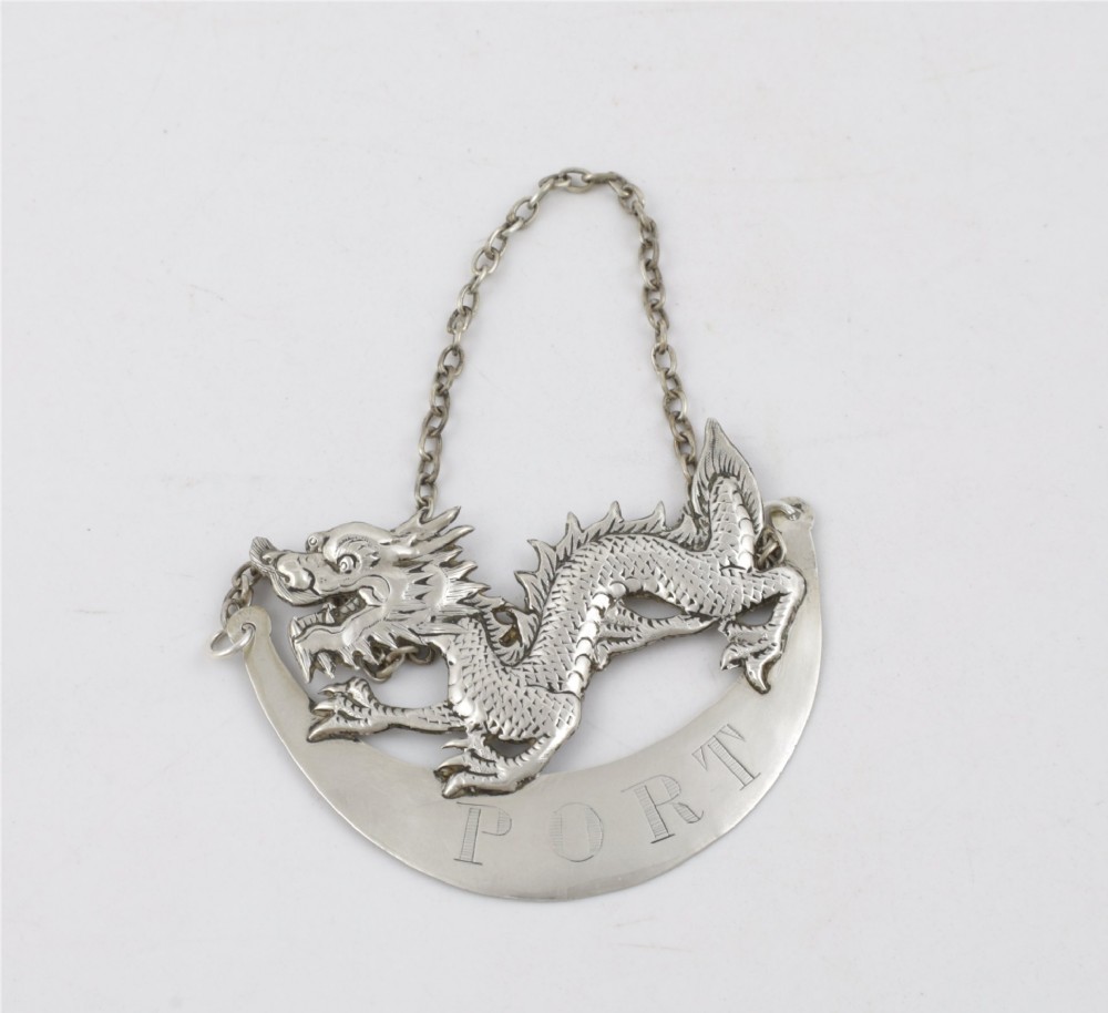 An antique Chinese silver decanter label depicting a chased dragon above a crescent plaque engraved with PORT, attached to a chain. View III