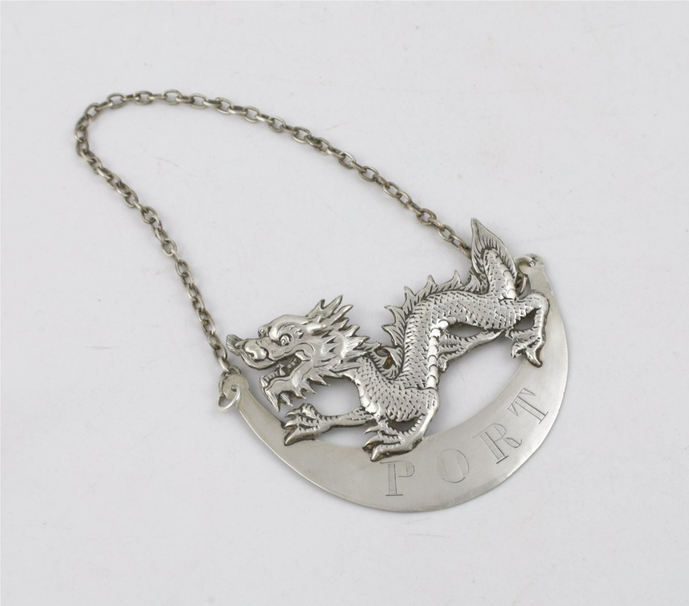An antique Chinese silver decanter label depicting a chased dragon above a crescent plaque engraved with PORT, attached to a chain. View IV
