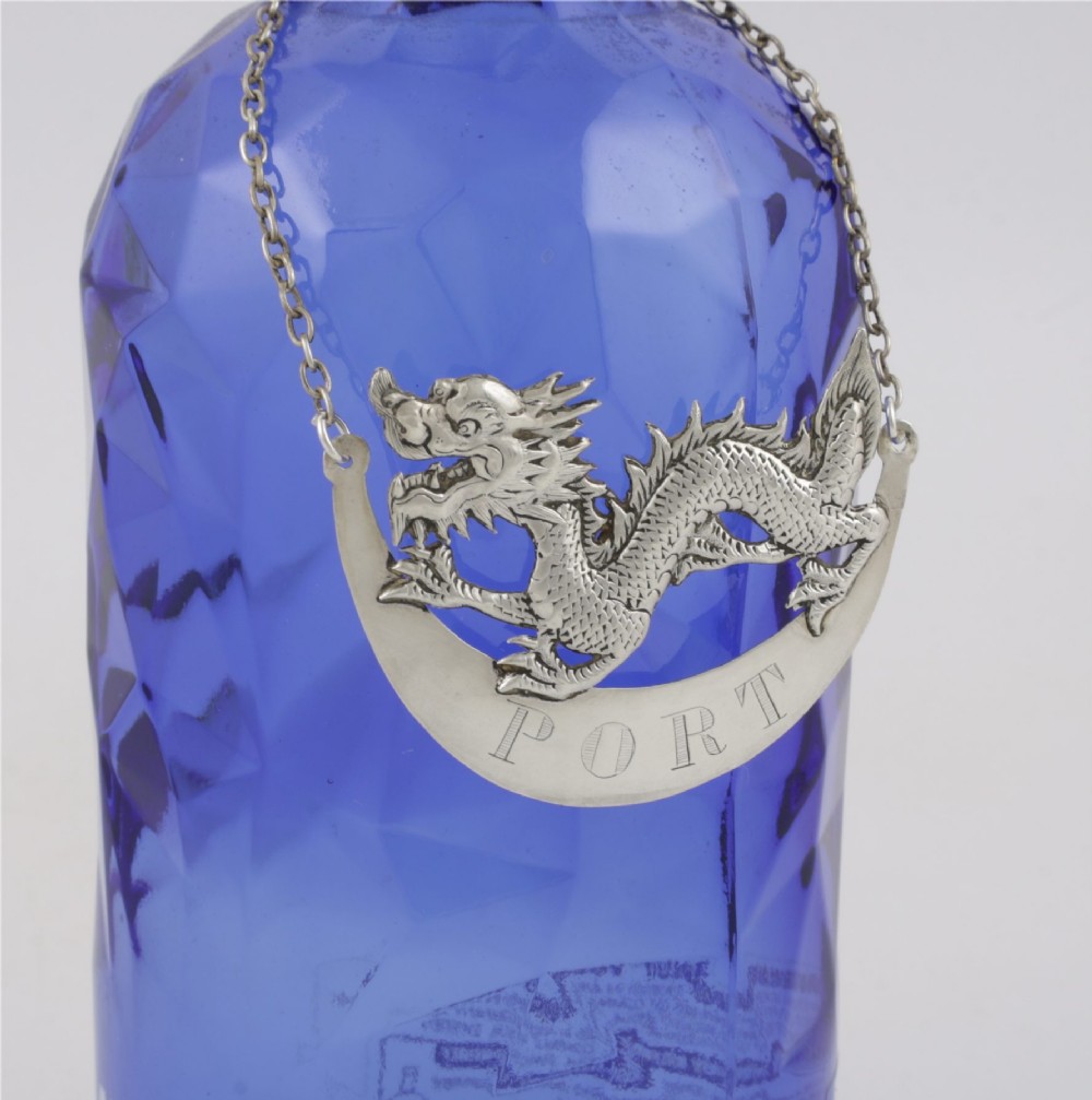 An antique Chinese silver decanter label depicting a chased dragon above a crescent plaque engraved with PORT, attached to a chain. View V