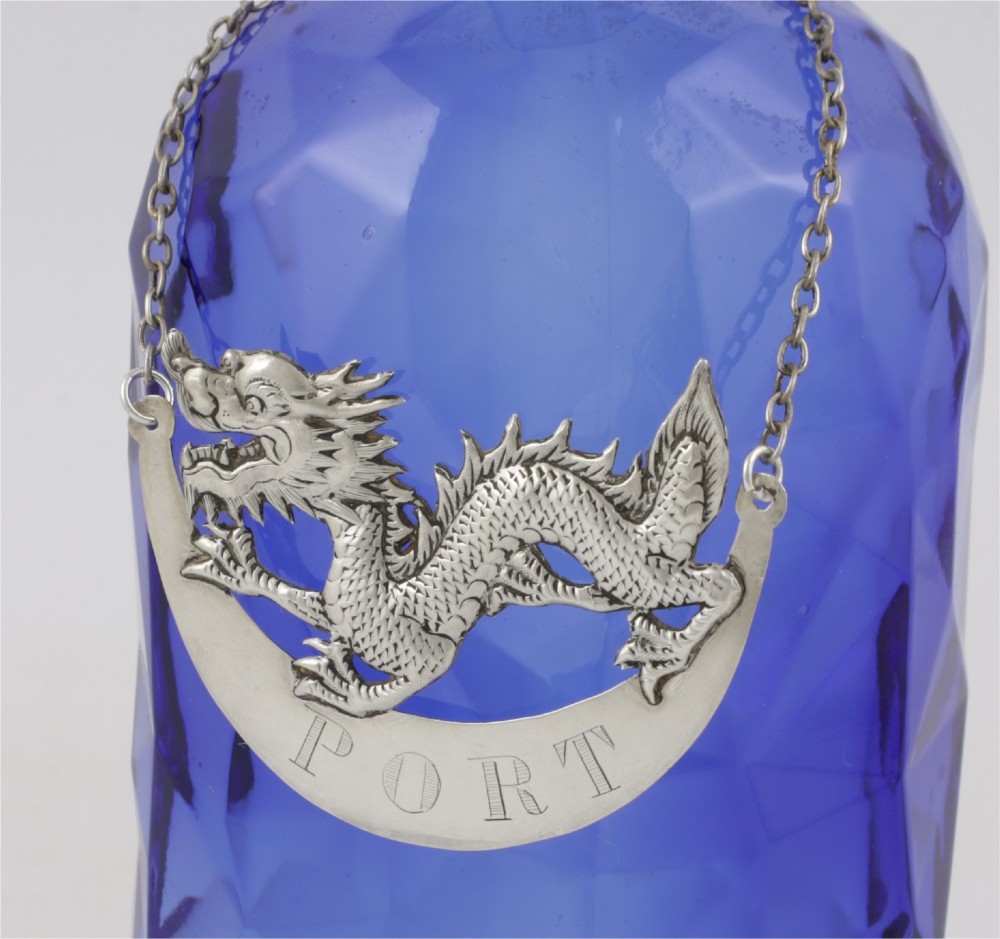 An antique Chinese silver decanter label depicting a chased dragon above a crescent plaque engraved with PORT, attached to a chain. View VI