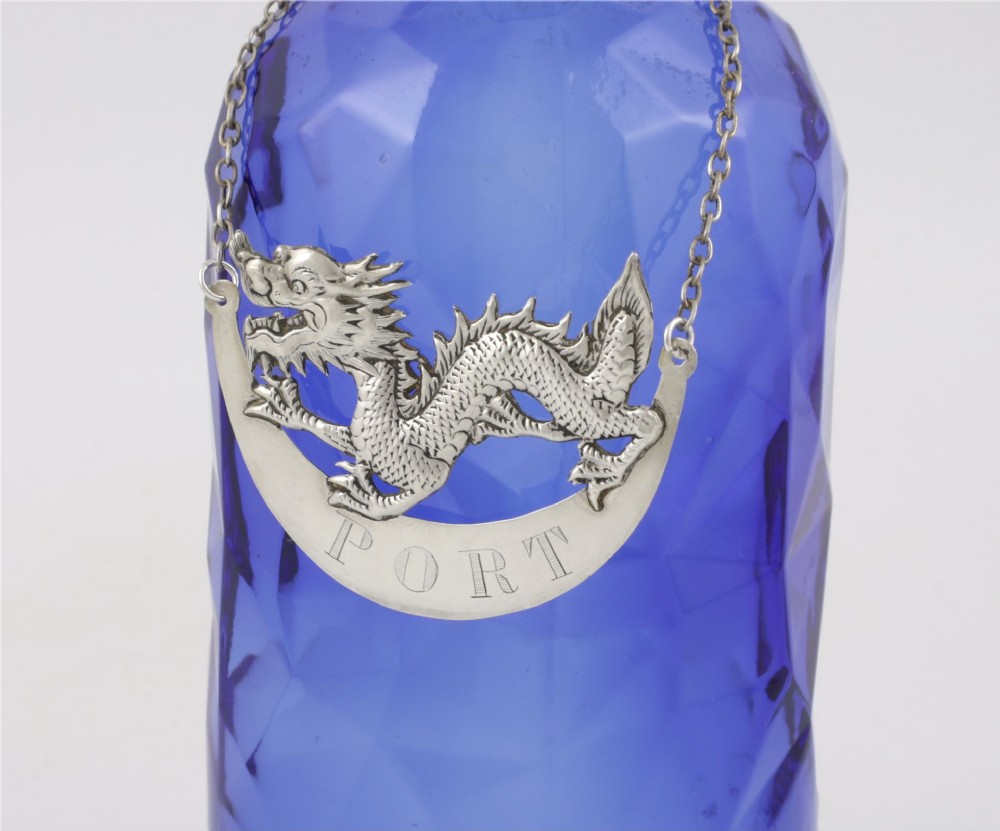 An antique Chinese silver decanter label depicting a chased dragon above a crescent plaque engraved with PORT, attached to a chain. View VIII