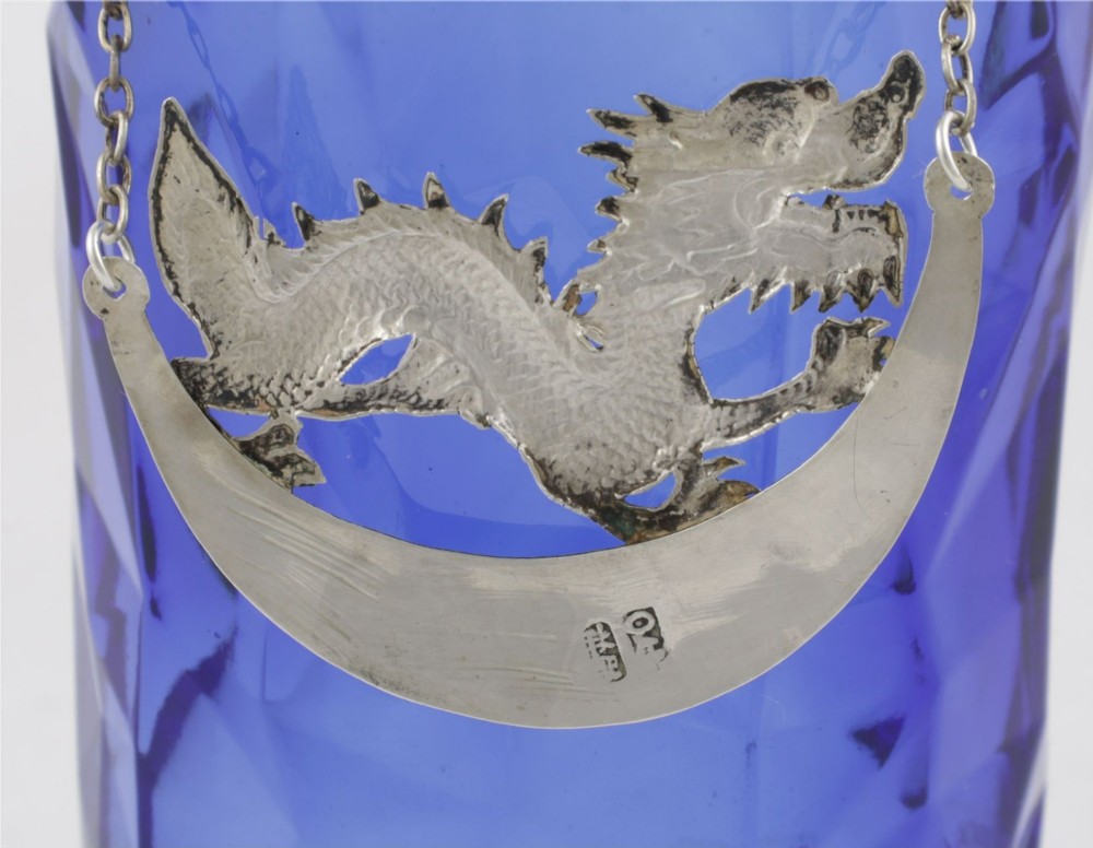 An antique Chinese silver decanter label depicting a chased dragon above a crescent plaque engraved with PORT, attached to a chain. View IX