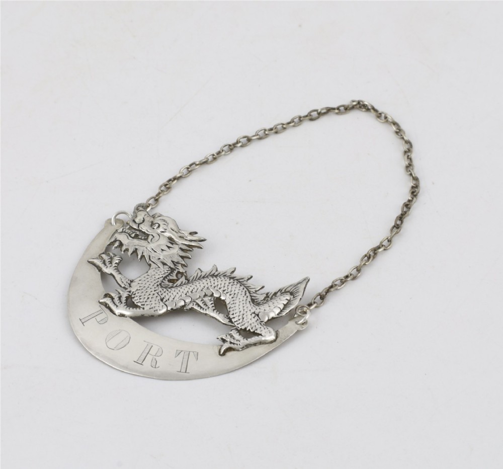 An antique Chinese silver decanter label depicting a chased dragon above a crescent plaque engraved with PORT, attached to a chain. View X