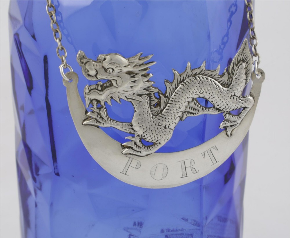 An antique Chinese silver decanter label depicting a chased dragon above a crescent plaque engraved with PORT, attached to a chain. View XI