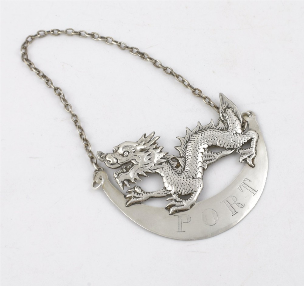 An antique Chinese silver decanter label depicting a chased dragon above a crescent plaque engraved with PORT, attached to a chain. View XII
