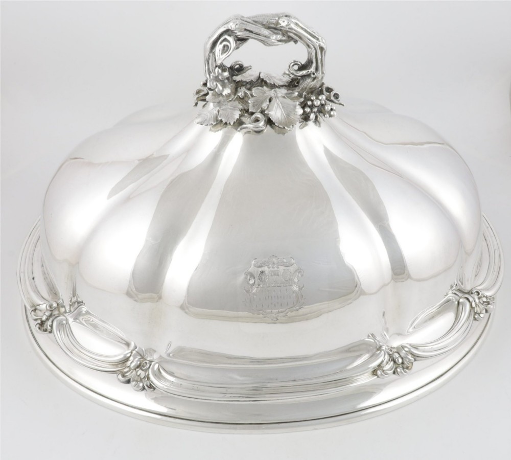 A Georgian Old Sheffield plate silver meat dome featuring a fluted body, an engraved heraldic coat of arms, and a cast handle adorned with vine leaves and grapes.
