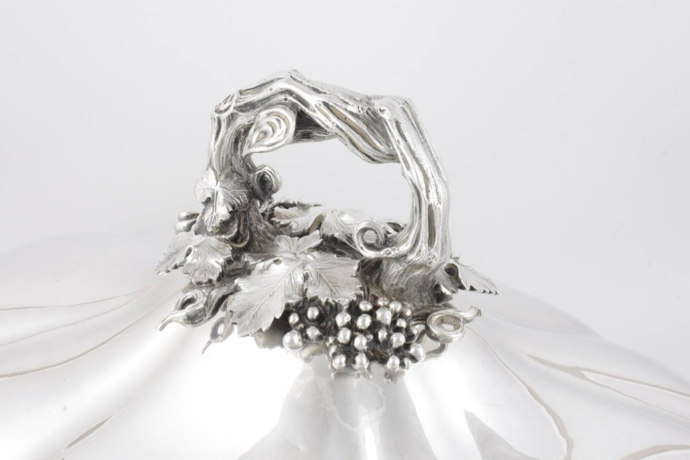 A Georgian Old Sheffield plate silver meat dome featuring a fluted body, an engraved heraldic coat of arms, and a cast handle adorned with vine leaves and grapes. View V