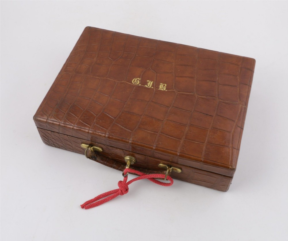 An open brown crocodile leather jewellery case featuring a green velvet lined interior with multiple compartments and brass lock hardware. View V