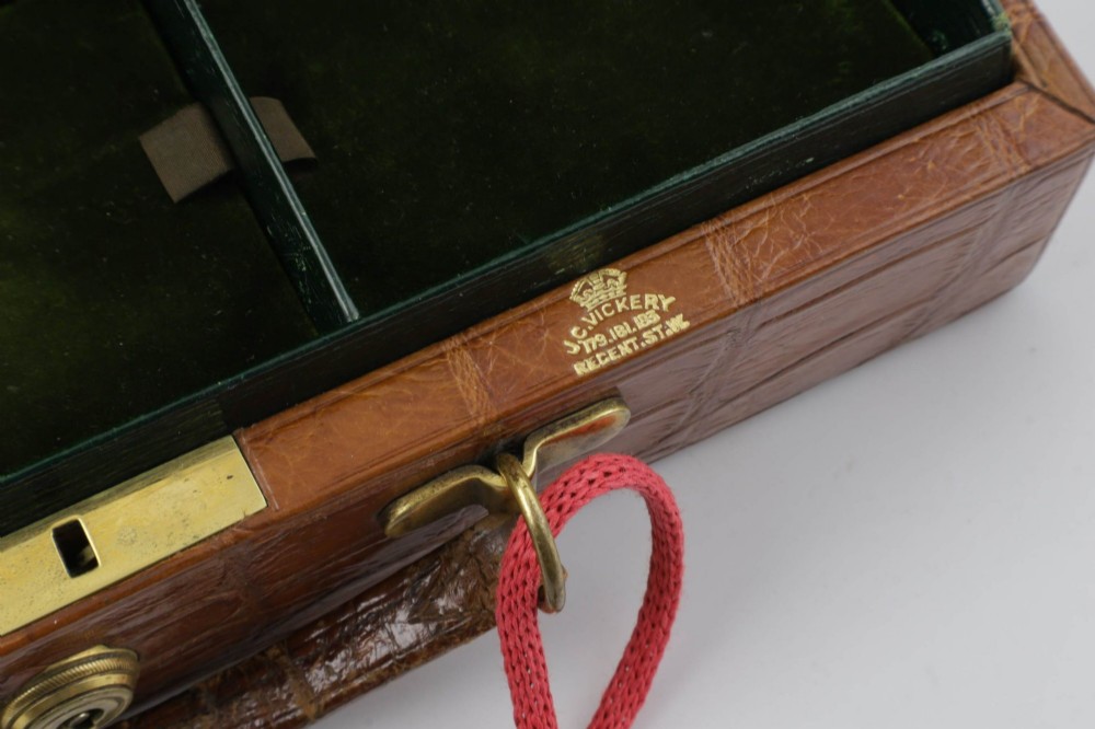 An open brown crocodile leather jewellery case featuring a green velvet lined interior with multiple compartments and brass lock hardware. View VI