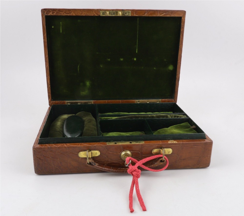 An open brown crocodile leather jewellery case featuring a green velvet lined interior with multiple compartments and brass lock hardware. View IX