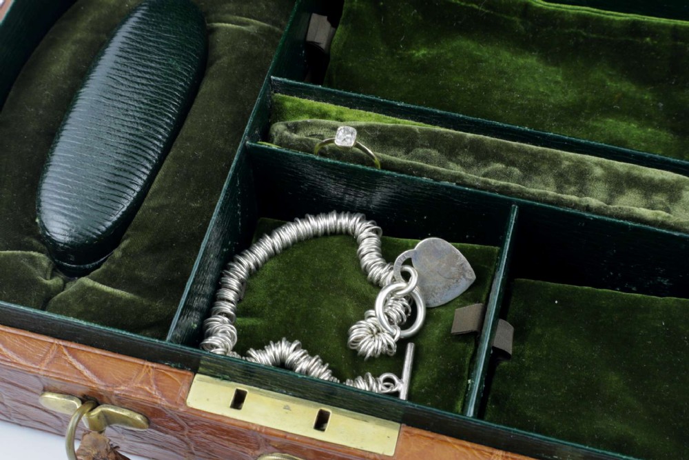 An open brown crocodile leather jewellery case featuring a green velvet lined interior with multiple compartments and brass lock hardware. View X