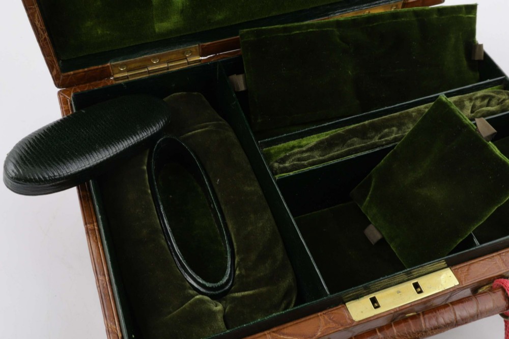 An open brown crocodile leather jewellery case featuring a green velvet lined interior with multiple compartments and brass lock hardware. View XI