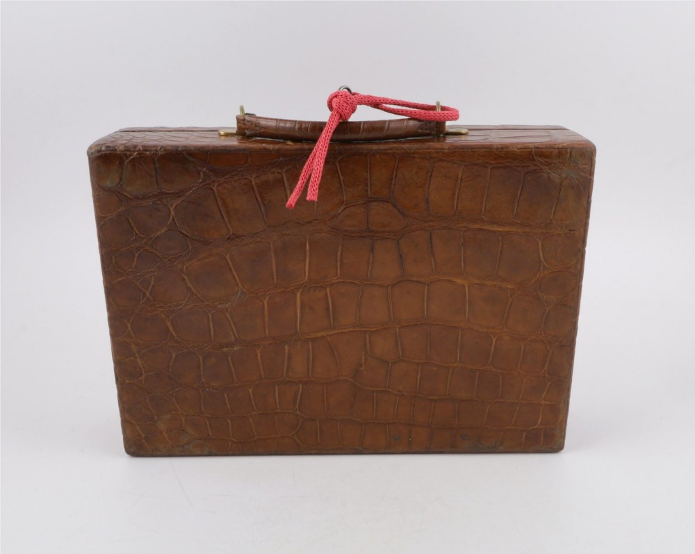An open brown crocodile leather jewellery case featuring a green velvet lined interior with multiple compartments and brass lock hardware. View XII