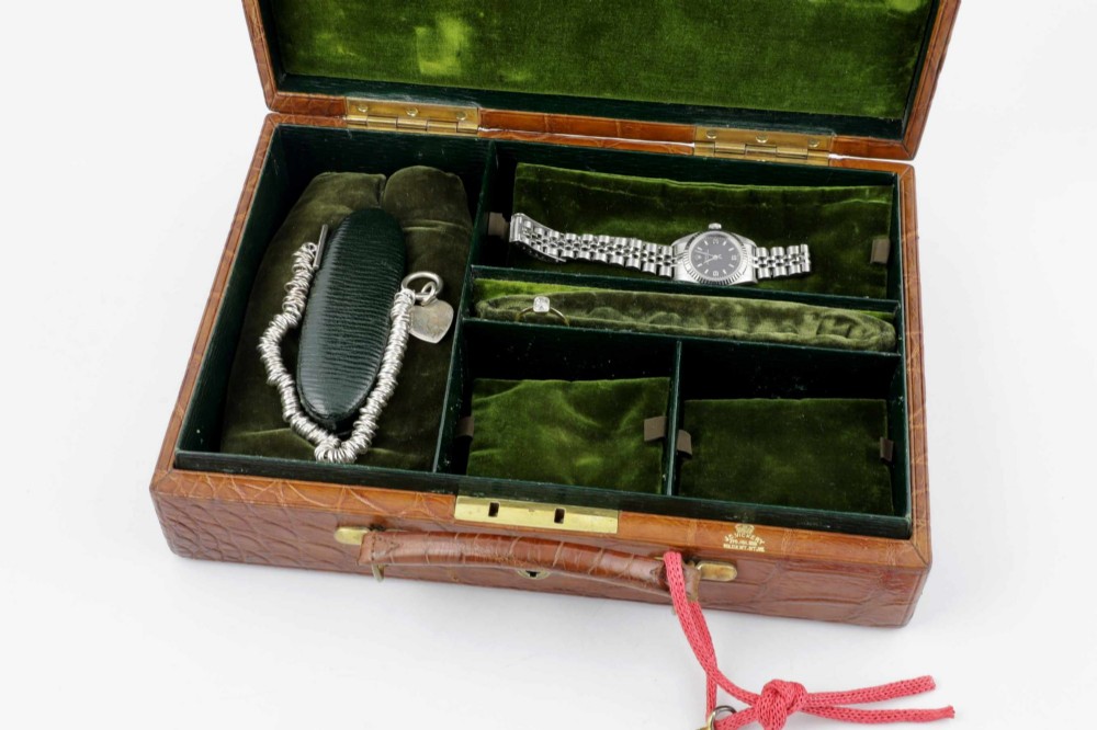 An open brown crocodile leather jewellery case featuring a green velvet lined interior with multiple compartments and brass lock hardware. View XV