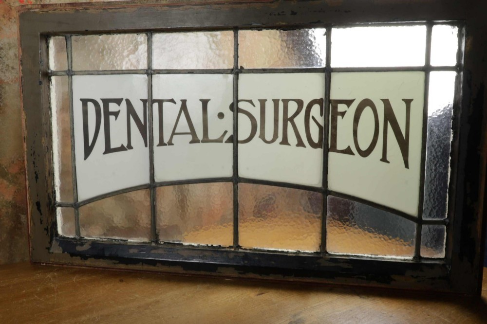 An Edwardian leaded glass window panel set in a dark wooden frame with white glass panes featuring black lettering that reads DENTAL SURGEON. View IV