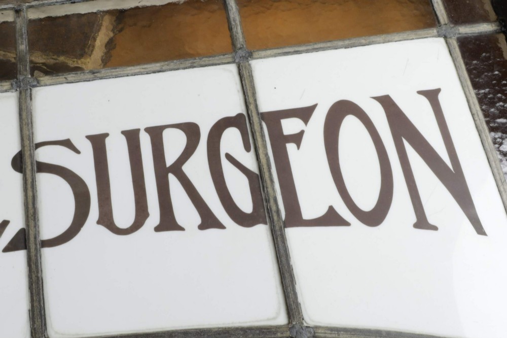 An Edwardian leaded glass window panel set in a dark wooden frame with white glass panes featuring black lettering that reads DENTAL SURGEON. View VI