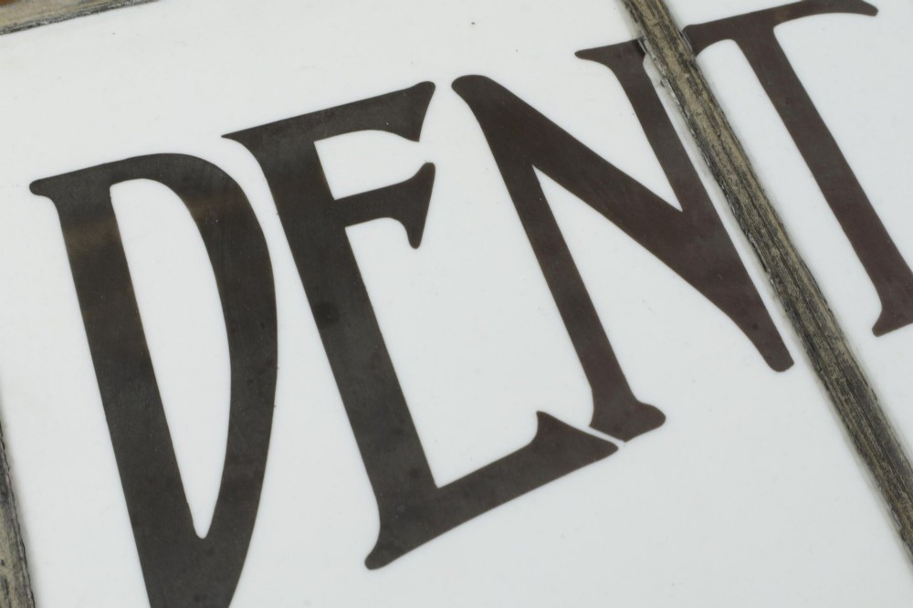 An Edwardian leaded glass window panel set in a dark wooden frame with white glass panes featuring black lettering that reads DENTAL SURGEON. View IX