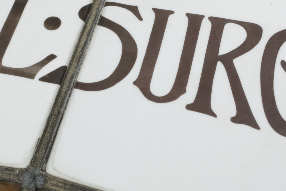 An Edwardian leaded glass window panel set in a dark wooden frame with white glass panes featuring black lettering that reads DENTAL SURGEON. View X