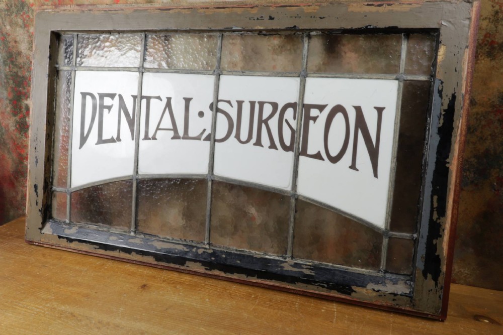 An Edwardian leaded glass window panel set in a dark wooden frame with white glass panes featuring black lettering that reads DENTAL SURGEON. View XIII