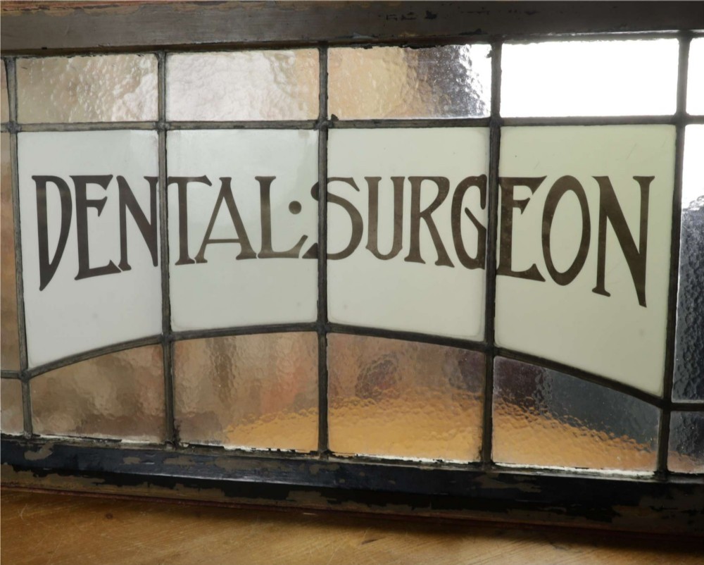 An Edwardian leaded glass window panel set in a dark wooden frame with white glass panes featuring black lettering that reads DENTAL SURGEON. View XIV