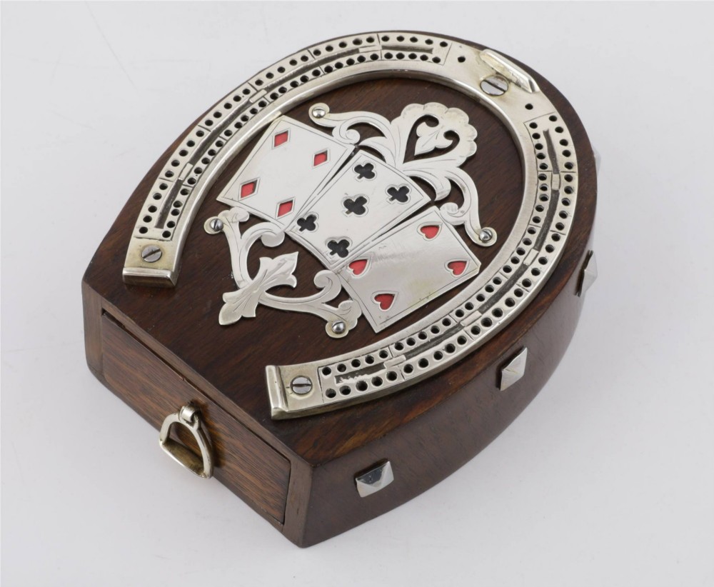 An antique horseshoe-shaped dark oak games box featuring silver metal scrollwork, playing card motifs, and an integrated cribbage scoring track.