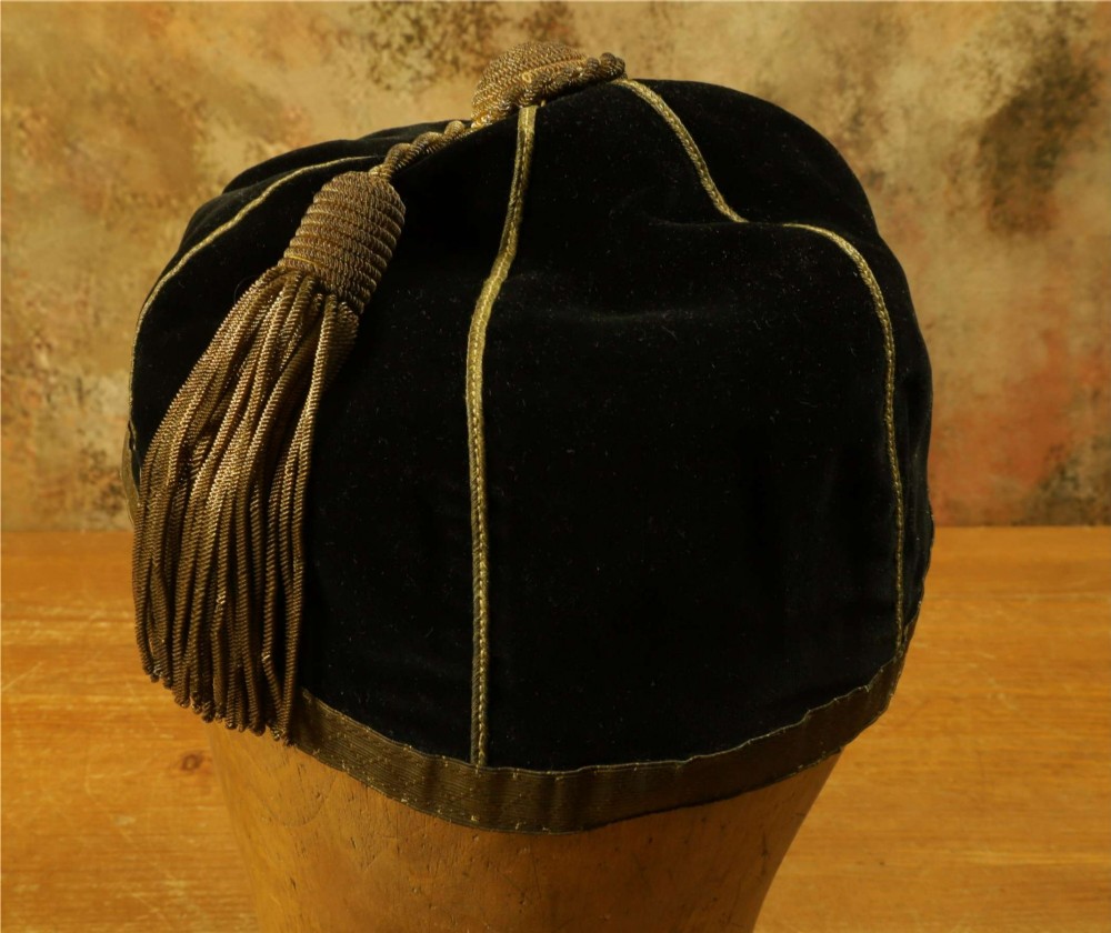 A 1920s black velvet sports cap featuring metallic braid piping, embroidered dates, monogram crest, and a prominent hanging tassel. View XI